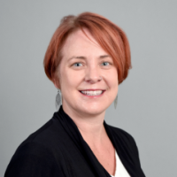 Redhead in black suit in front of gray background